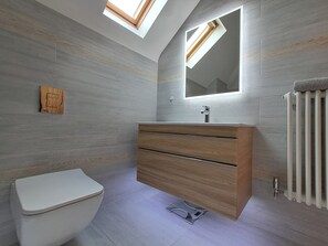 Een moderne badkamer met dakraam, een houten wastafelmeubel en een wit toilet.