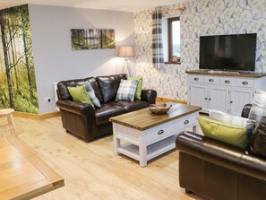 Een woonkamer met een bruine leren bank, een houten salontafel en een televisie op een kast.