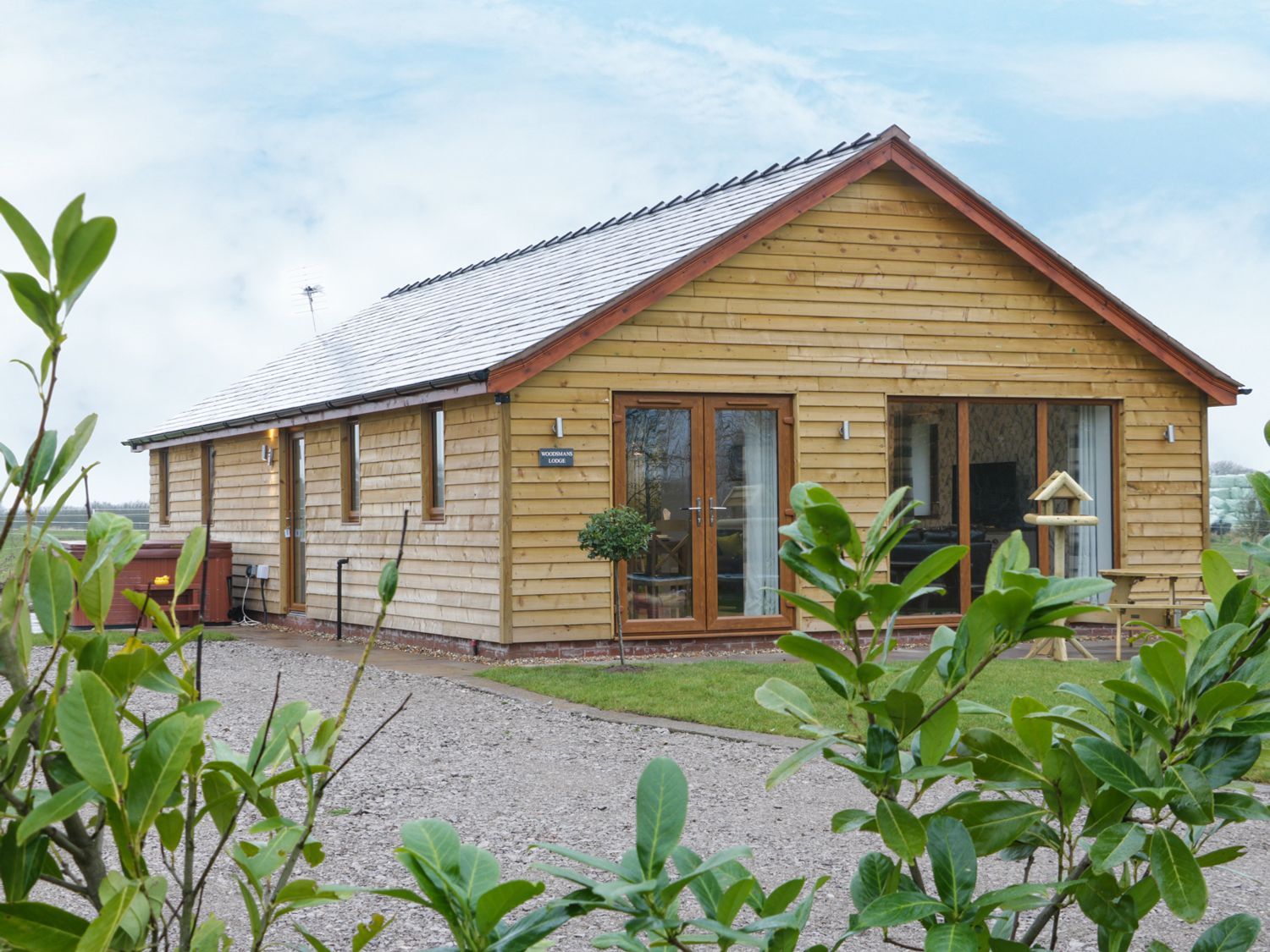 Een houten chalet met een schuin dak, grote ramen en een grindpad.