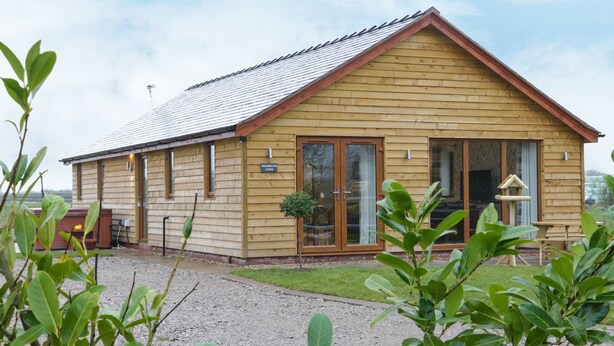 A wooden lodge with a pitched roof, large windows, and a gravel driveway. - WOODMAN'S LODGE, family friendly, with hot tub in Nantwich (Nantwich)