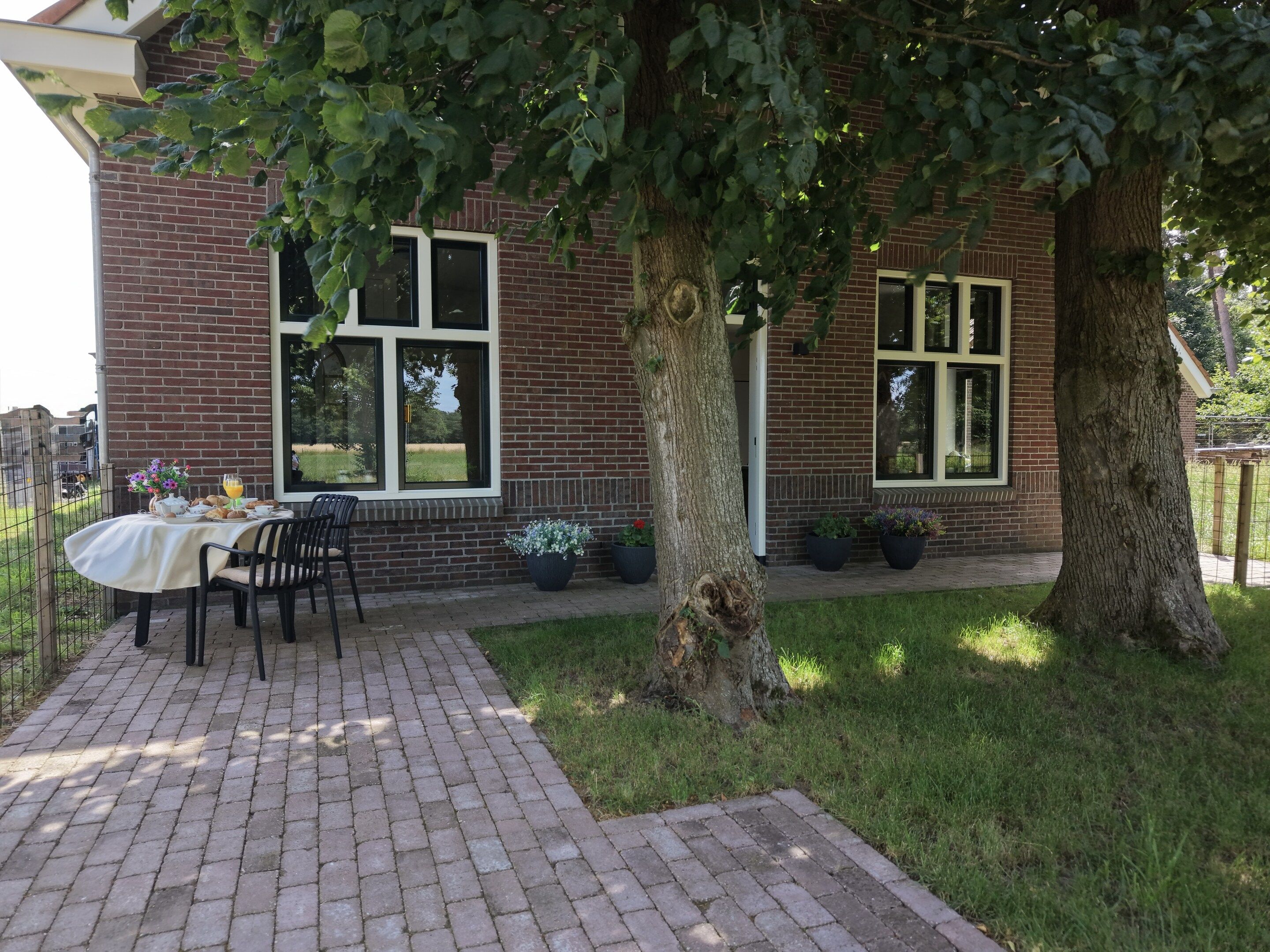 Een gebouw van baksteen met een tafel en stoelen buiten, omgeven door gras en bomen.