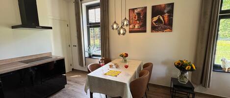 A dining area with a table set for four, a kitchen with a modern stove, and a window with curtains.