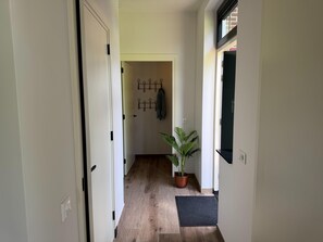 Ein Flur mit Holzboden, einem Blumentopf, einem Kleiderständer und einer Tür zu einem anderen Raum.