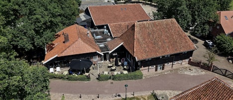 Een landelijk gebouw met een schuin dak, omringd door bomen en open velden.