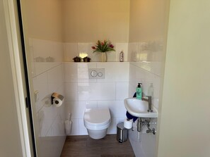 Un baño con inodoro, lavamanos y un cubo de basura.
