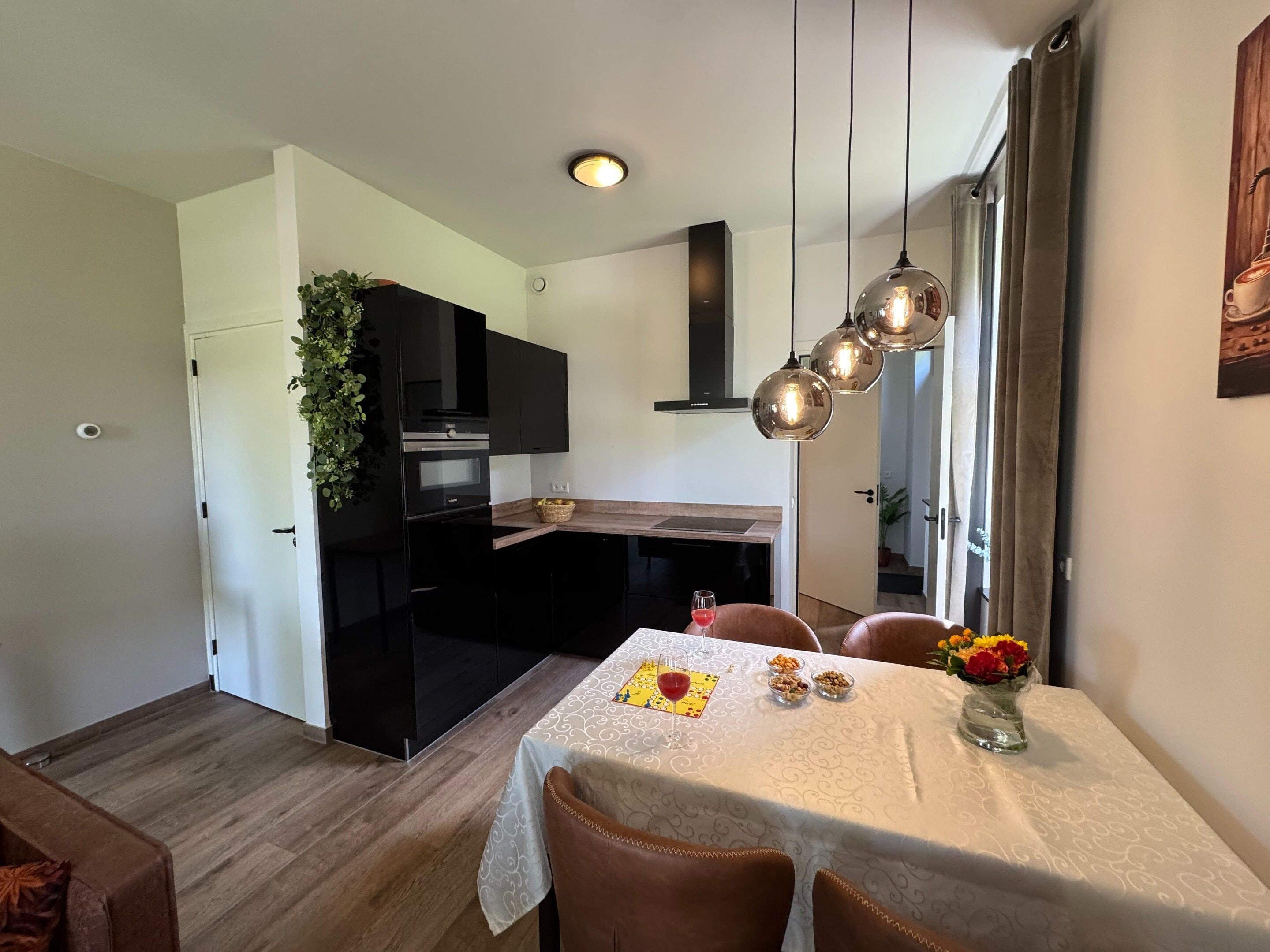 A modern kitchen with black cabinets, a built-in oven, and a dining area with a table set for two.