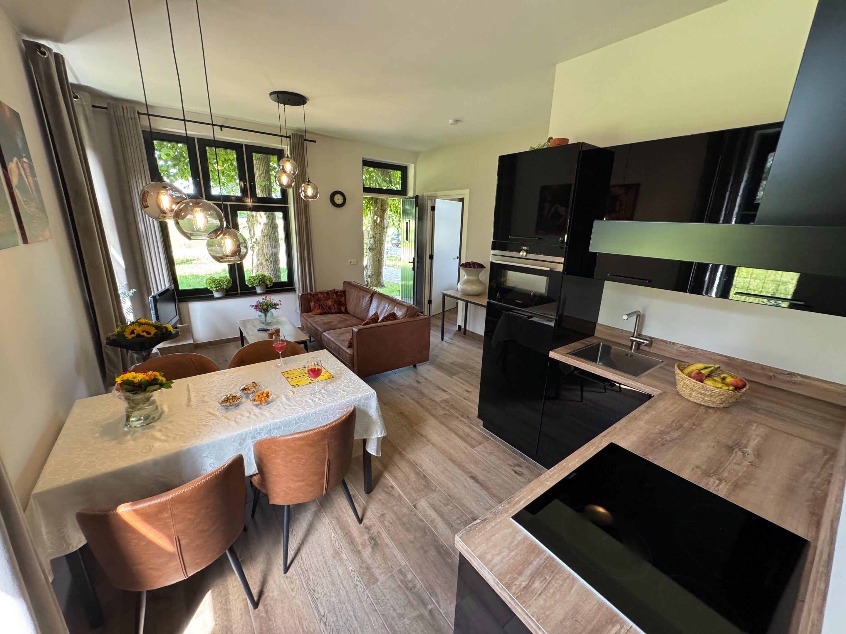 Une cuisine moderne avec un coin repas, comprenant un îlot central, un éclairage suspendu et une vue sur l’extérieur.