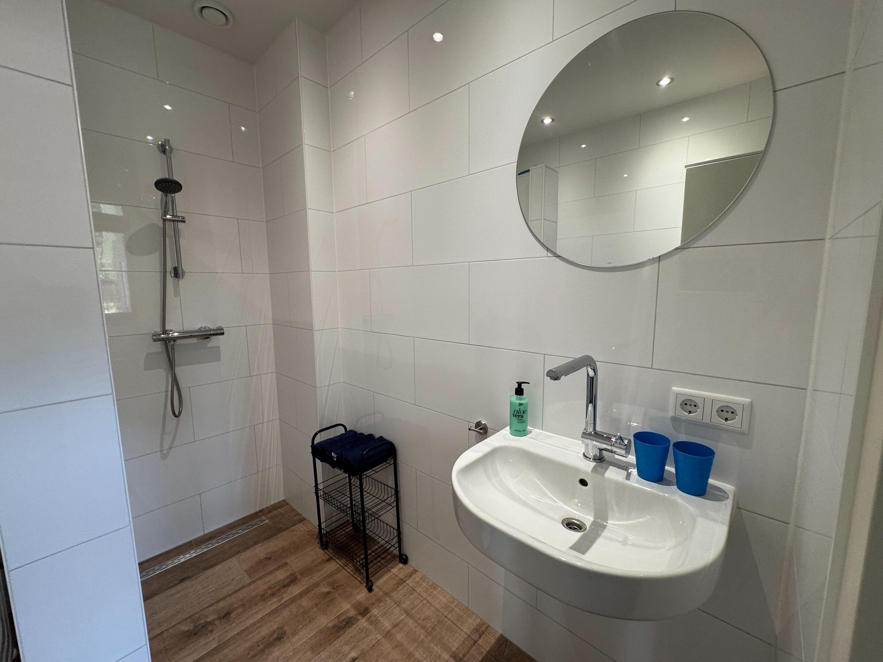 Ein Badezimmer mit Dusche, Waschbecken, Spiegel und einem kleinen Hocker.