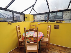 A room with a yellow wall, a wooden table with a colorful tablecloth, and a chair. There is a window with a view of the outside. - HUD Y COED, pet friendly, character holiday cottage in Llangynog (Oswestry)