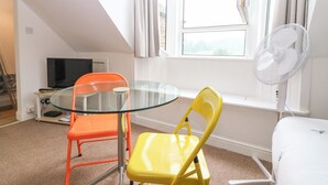 A room with a glass table, two chairs, a TV, a window with curtains, and a standing fan. - HILL VIEW STUDIO, with a garden in Hawick (Hawick)