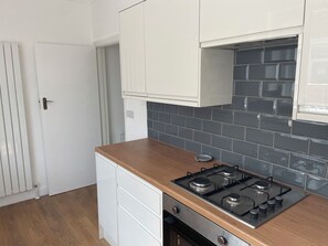 A kitchen with white cabinets, a gas stove, and a tiled backsplash. - SUMMER COTTAGE, pet friendly, with a garden in Rustington (Littlehampton)