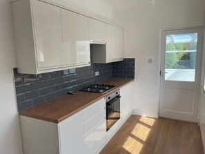 A modern kitchen with white cabinets, a black tiled backsplash, a wooden countertop, and a built-in oven. - SUMMER COTTAGE, pet friendly, with a garden in Rustington (Littlehampton)