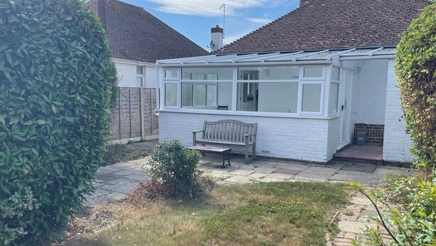 A white house with a conservatory, a wooden bench, and a garden. - SUMMER COTTAGE, pet friendly, with a garden in Rustington (Littlehampton)
