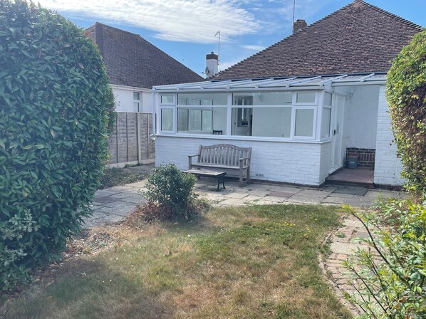 A white house with a conservatory, a wooden bench, and a garden. - SUMMER COTTAGE, pet friendly, with a garden in Rustington (Littlehampton)