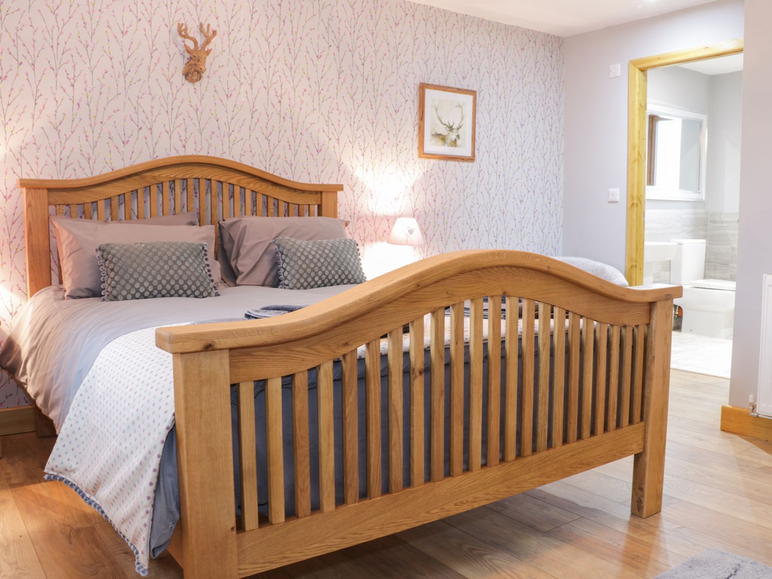 Een slaapkamer met een houten bed, behang met een patroon, een ingelijst schilderij aan de muur en een houten deurkozijn.
