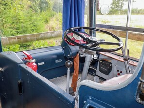 Ein Autobusinnenraum mit Lenkrad, Armaturenbrett und einem Fenster mit Blick auf Grünflächen.