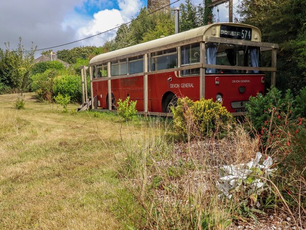 Ein roter Bus mit der Aufschrift 'DEVON GENERAL', geparkt in einer grünen Umgebung mit Vegetation.