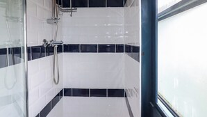 A bathroom with white and black tiled walls, a shower area, and a window.