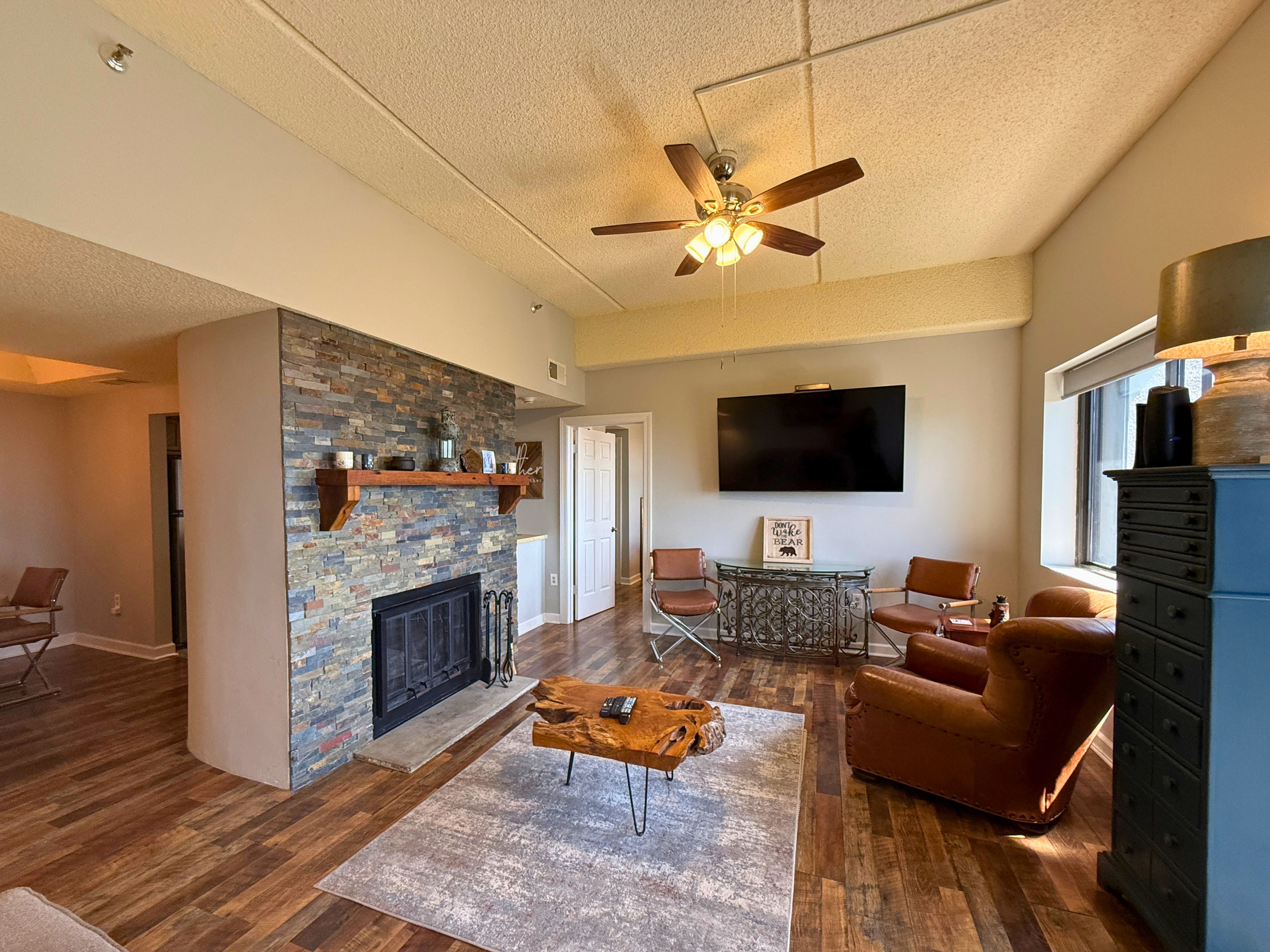 A spacious living room with a fireplace, a ceiling fan, a television, and leather sofas.