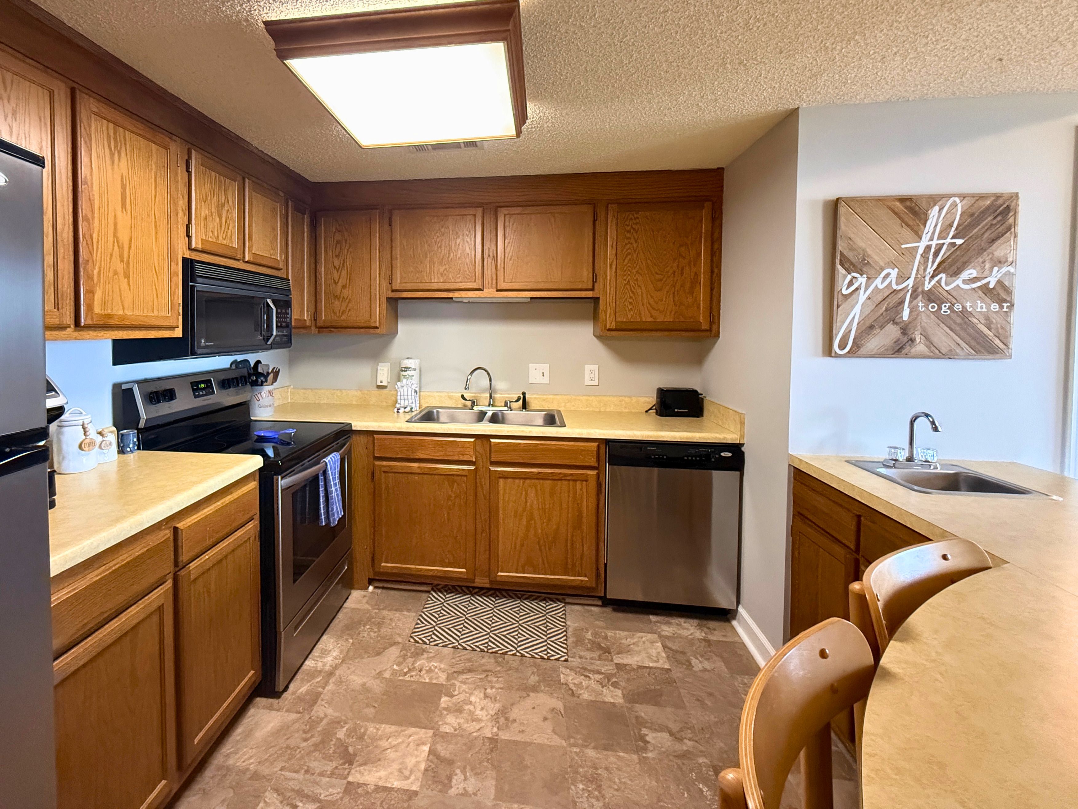 A kitchen with wooden cabinets, stainless steel appliances, a granite countertop, and a wall-mounted sign.