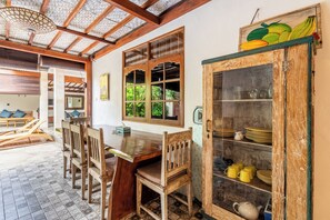 A traditional wooden dining area with a tiled floor, a wooden table, and chairs. There is a cabinet with glass doors containing dishes and a teapot. - Just a few min stroll to the Seminyak beach (Bali)