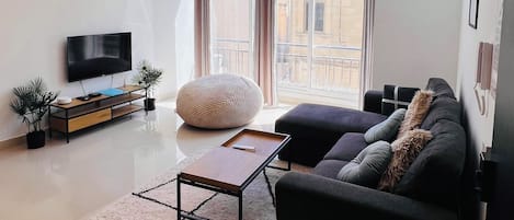 Una sala de estar moderna con un televisor de pantalla plana, un sofá, una mesa de centro y un ventanal con cortinas.