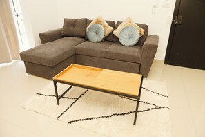 A sectional sofa with two pillows, a wooden coffee table, and a white rug with black lines. - St. Julian's Central Apartment 3 (St. Julian's)