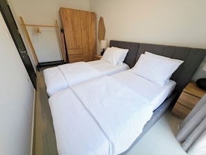 Una cama doble con ropa de cama blanca, un armario de madera, una mesita de noche con una lámpara y un espejo en la pared.