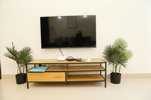 A flat-screen TV mounted on a wall above a wooden TV stand with two potted plants on either side. - St. Julian's Central Apartment 3 (St. Julian's)
