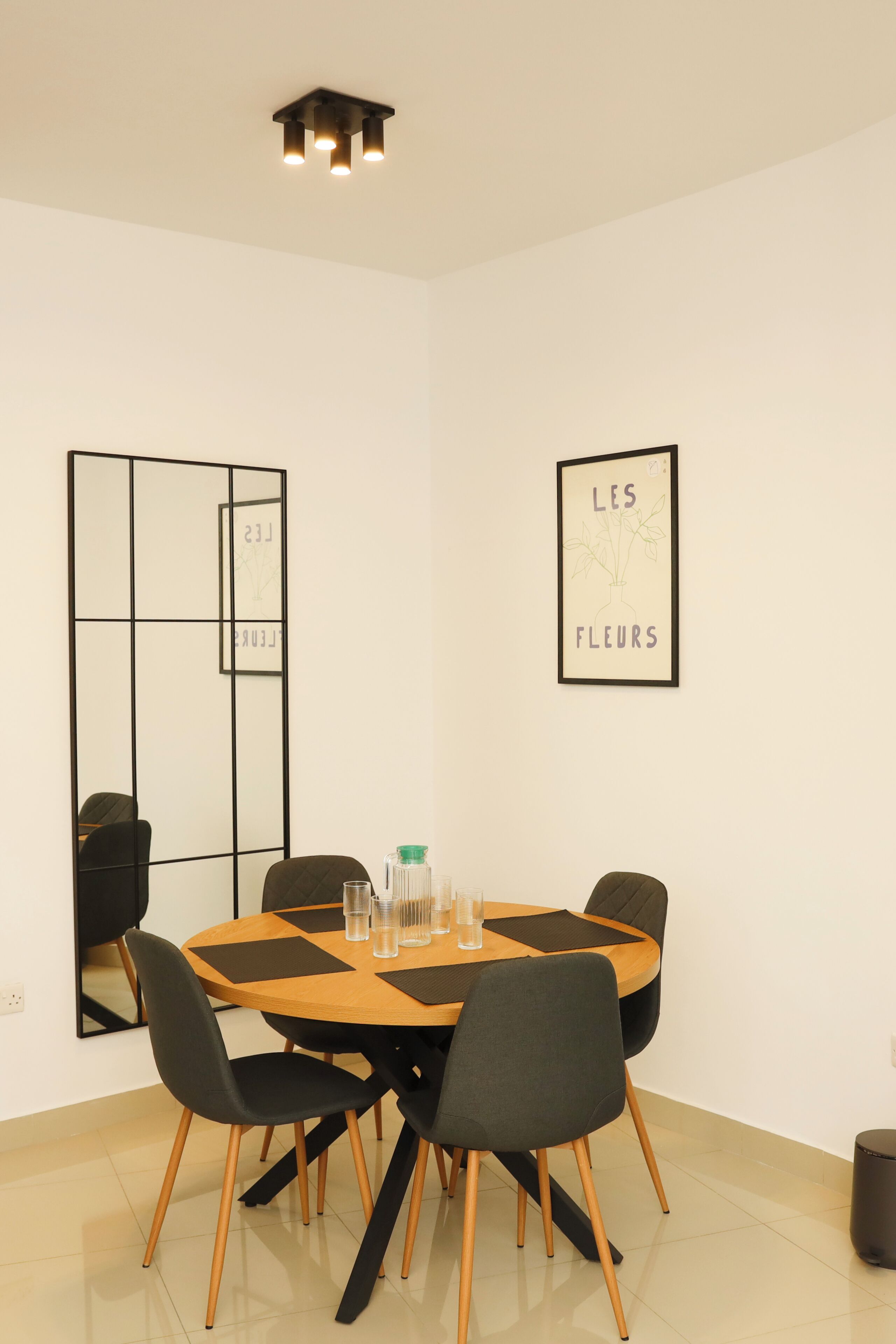 Un comedor moderno con una mesa redonda, cuatro sillas y una obra de arte enmarcada en la pared.