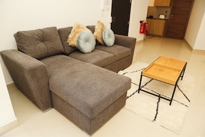 A sectional sofa with two pillows, a small wooden side table, and a white rug in a living room. - St. Julian's Central Apartment 3 (St. Julian's)