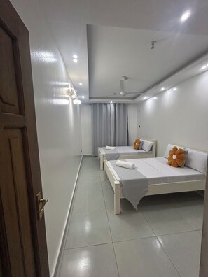 A hotel room with two beds, a ceiling fan, and a door. - A stylish, family friendly 2 bedroom bnb with pool and 3 mins to the beach. (Mombasa)