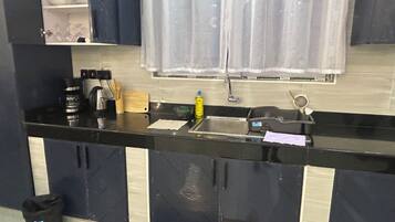 Une cuisine avec un plan de travail noir, un évier, des placards et une fenêtre avec un rideau.