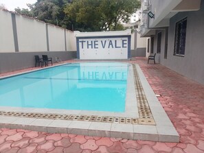 En swimmingpool med en skylt som visar texten ”THE VALE” och en stenlagd gångväg med stolar.