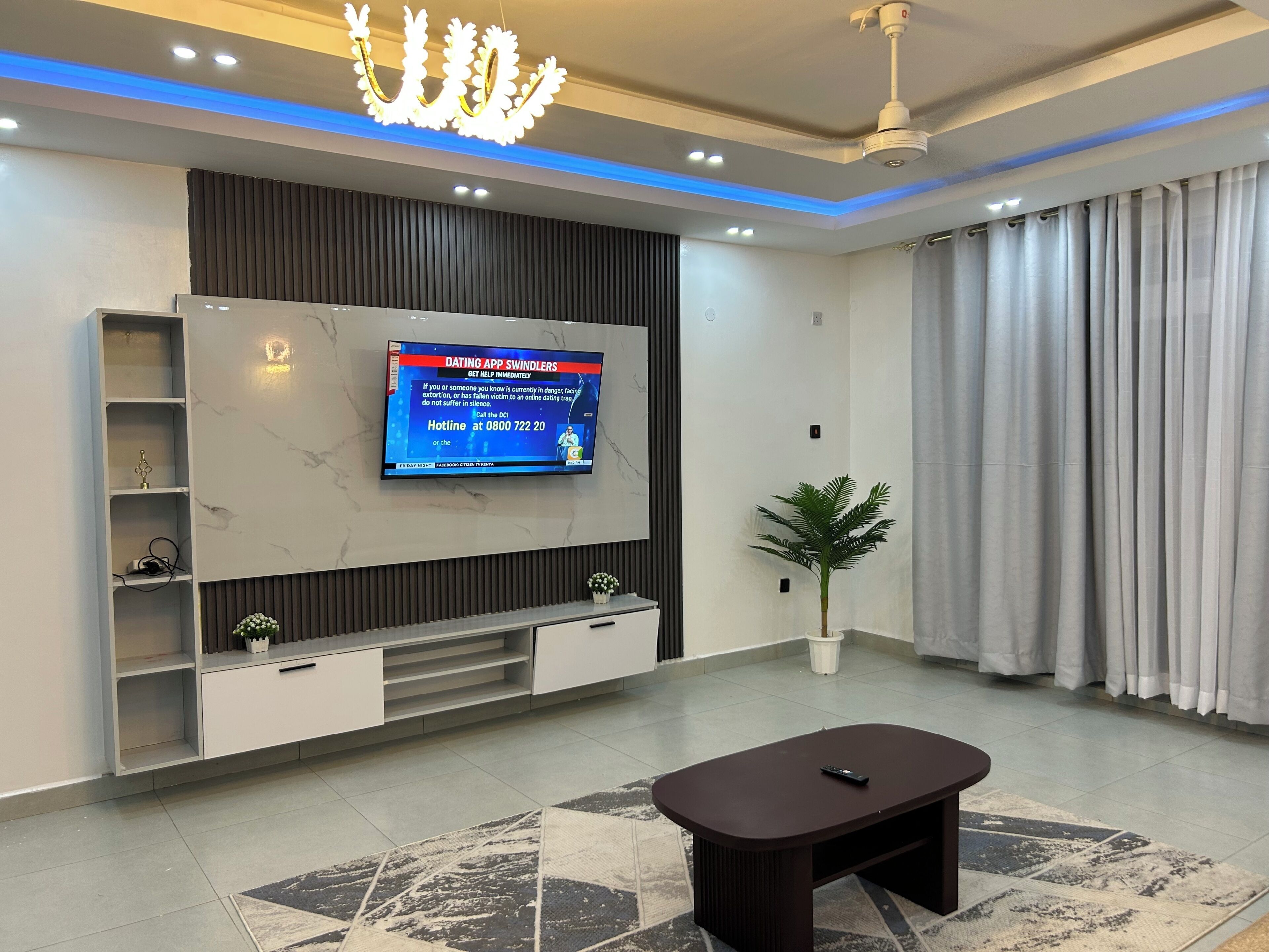 Een moderne woonkamer met een flatscreen televisie aan een muur, een salontafel en een potplant.