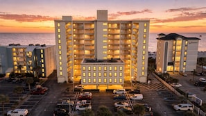 Un hôtel à plusieurs étages doté d’une cour intérieure, d’un parking et offrant une vue sur l’océan au coucher du soleil.