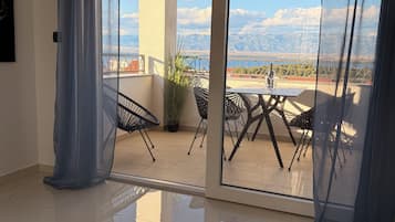 Habitación con vistas a montañas y un puente, un balcón con sillas y una mesa, y un ventanal corredero.