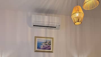 Un dormitorio con una cama grande, dos almohadones decorativos, un cuadro enmarcado en la pared, un equipo de aire acondicionado y tres lámparas colgantes.