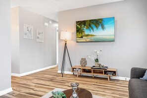 A modern living room with a wooden floor, a large painting of a beach, a floor lamp, and a console table with decorative items.