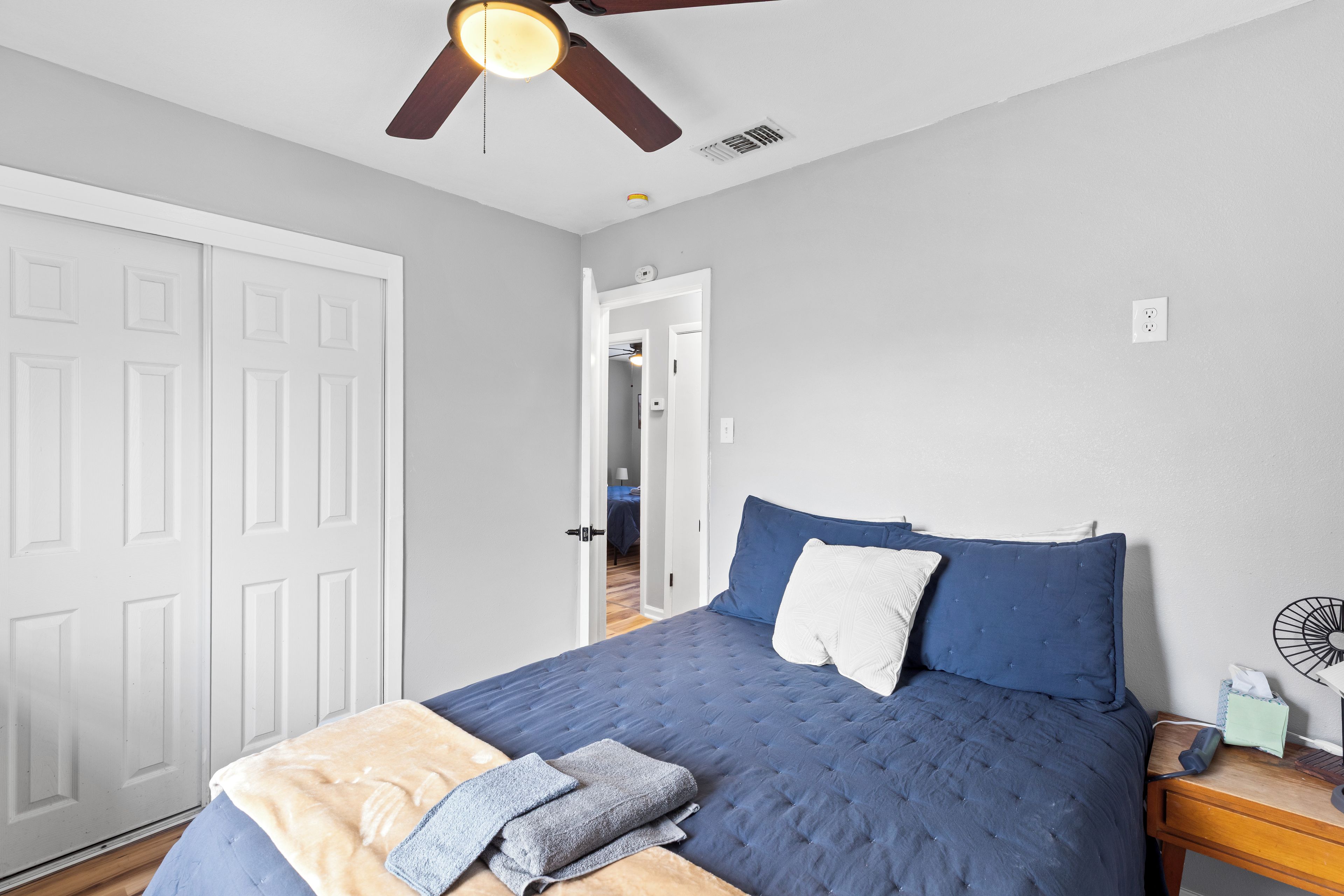 A bedroom with a bed, a bedside table, a ceiling fan, and a door.