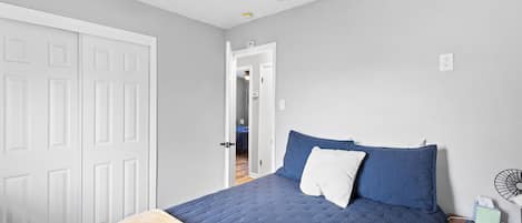 A bedroom with a bed, a bedside table, a ceiling fan, and a door.