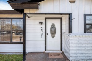 Uma casa branca com o número 2301 na porta, um tapete de boas-vindas e uma caixa de correio.