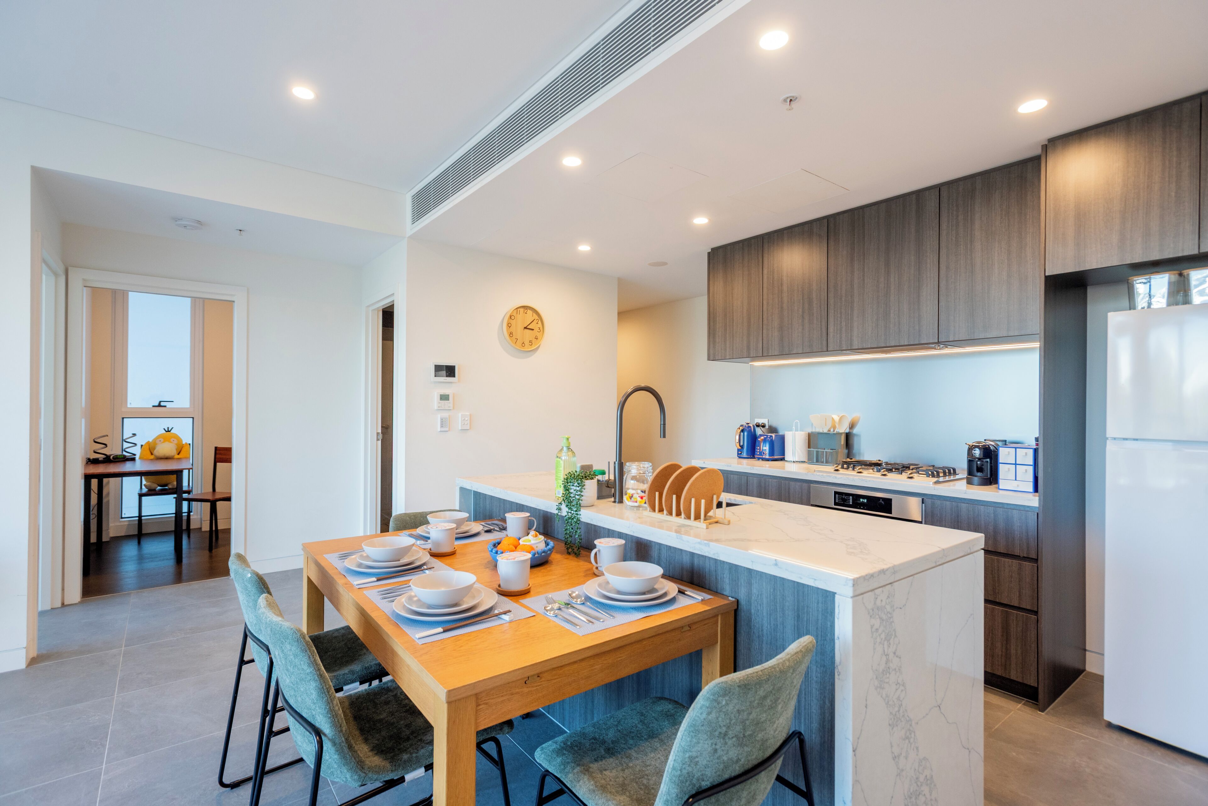 Een moderne keuken met een centraal eiland, inbouwapparatuur en een eethoek met een tafel voor vier personen.