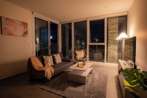 A modern living room with a sofa, coffee table, and a large window with a city view. - Stadium View (Lidcombe)
