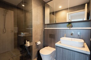 A modern bathroom with a glass-enclosed shower, a white sink, and a toilet. - Stadium View (Lidcombe)