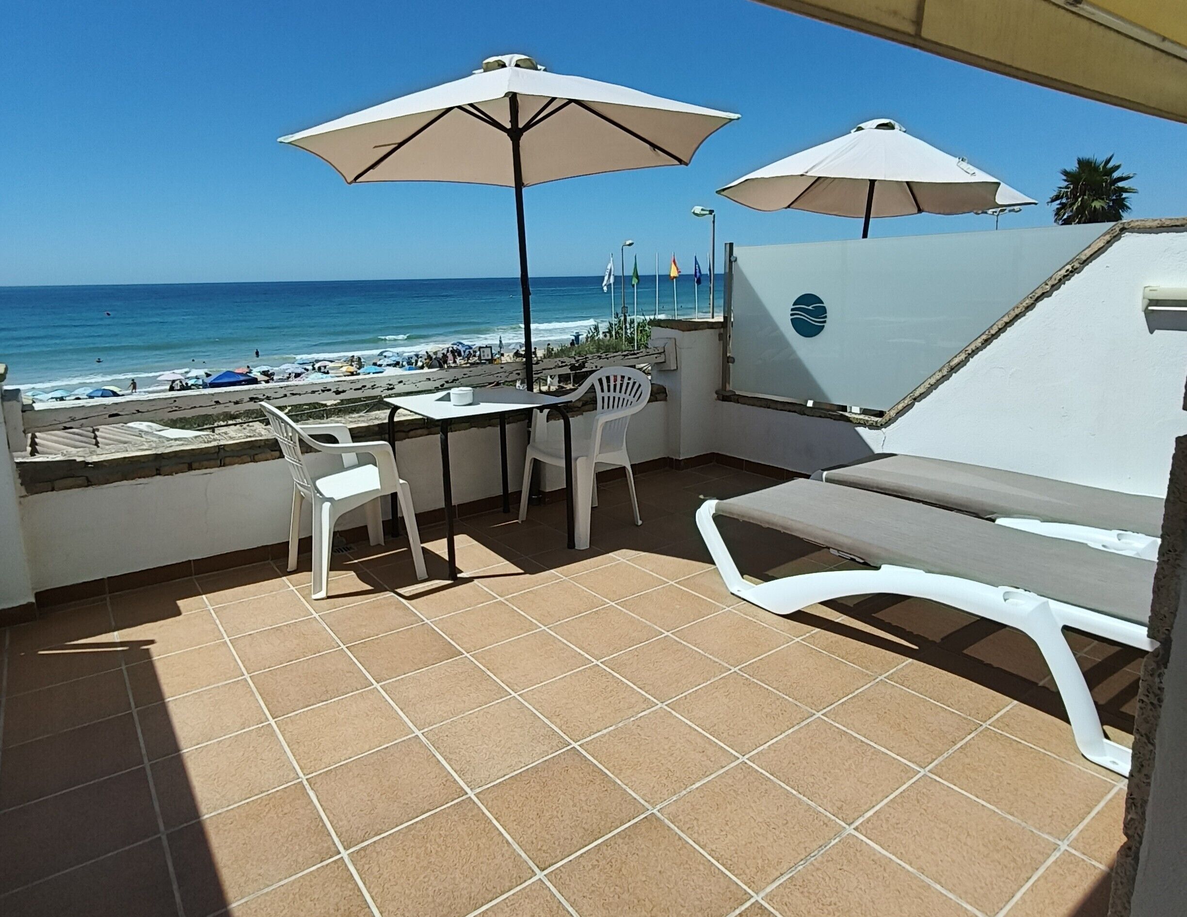 A terrace with a view of the beach, white outdoor furniture, and umbrellas.
