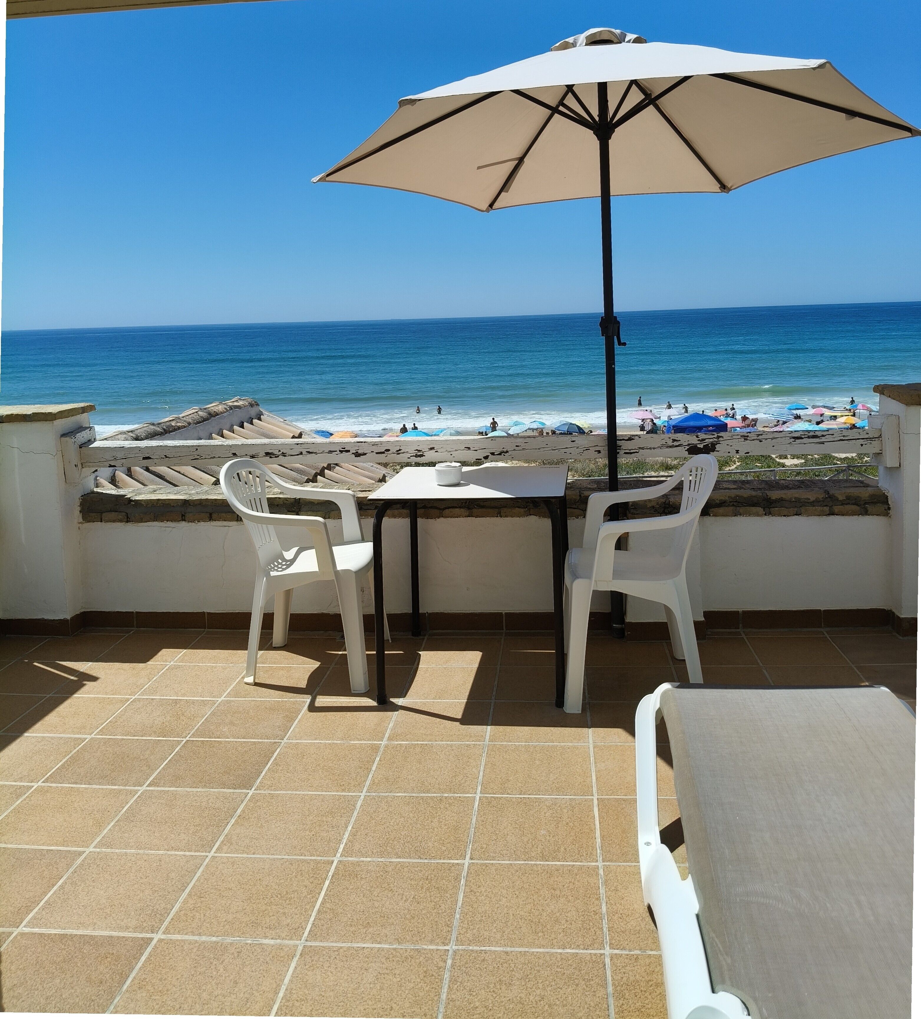 A terrace with a table and chairs, a beach view, and a large umbrella.