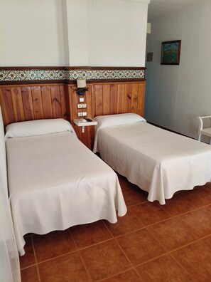 A hotel room with two beds, a wooden headboard, a small table with a lamp, and a tiled floor. - Hostal Casa Francisco el de siempre (Vejer de la Frontera)