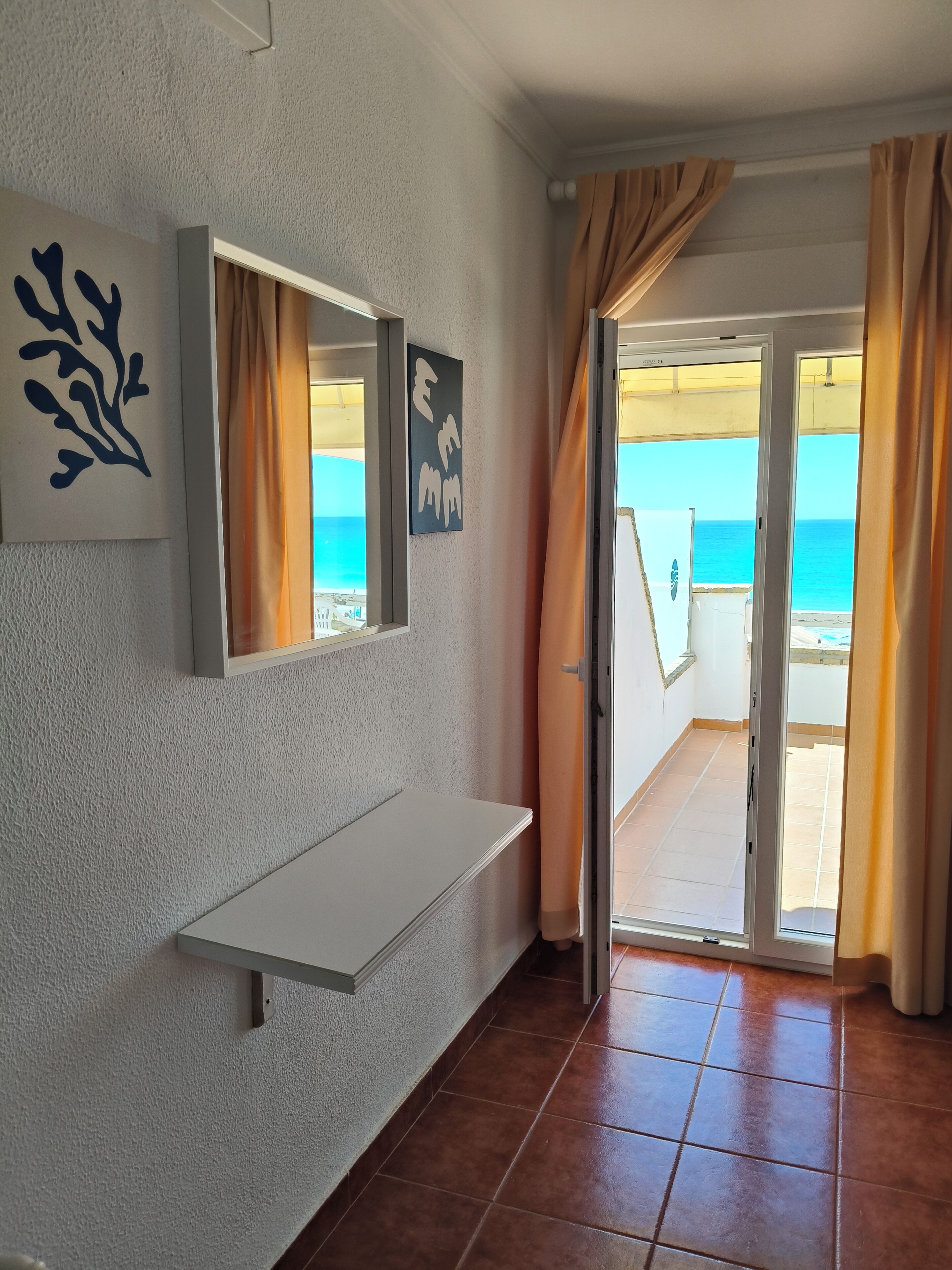Una habitación con un banco blanco, un espejo fijado a la pared y vista al mar a través de un ventanal.