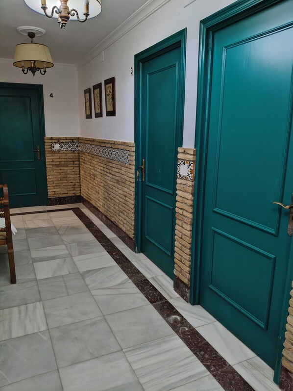 A hallway with teal doors, a chandelier, and a patterned wall.